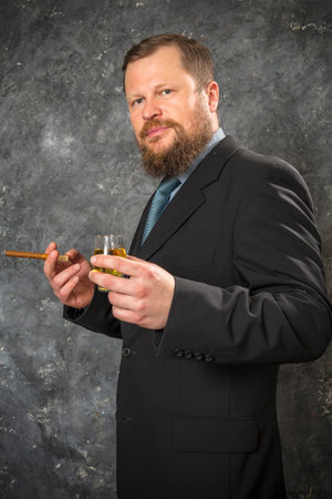 Solid confident bearded man in suit with glass of whisky and cigarの写真素材