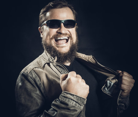 Emotional bearded man in sunglasses dressed in leather jacket is happy to winの写真素材