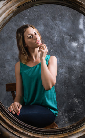 Beautiful young woman looking on her reflection at the mirrorの写真素材