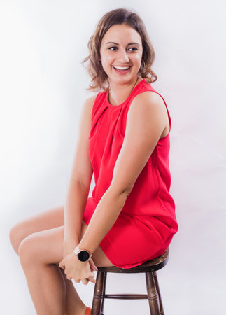 Beautiful young positive woman in red dress sitting on high chairの写真素材