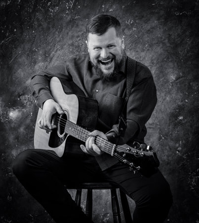 Mature musician plays acoustic guitar emotional studio portrait.の写真素材