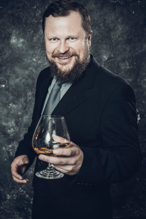 Solid smiling bearded man in suit with glass of whiskyの写真素材