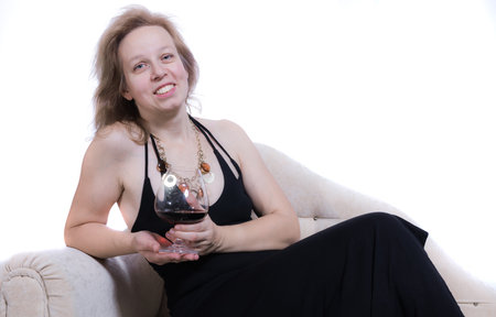 Cheerful 40 years old woman in black dress having relax on sofa with glass of wineの写真素材