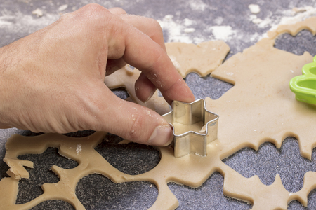 man prepares the dough and bakes gingerbread and cookies in the kitchen. He makes a star shape on the dough.の写真素材
