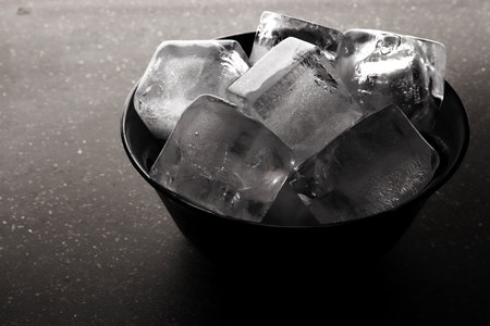 Black bowl filled to the brim with ice cubesの写真素材