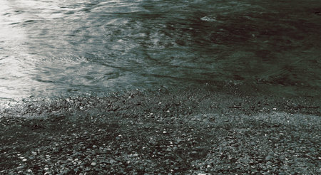 A close-up view of a rivers edge, where the clear, rippling water meets a bed of smooth, gray...
