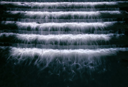 A close-up of a cascading waterfall flowing over steps of a dam in the late evening.
