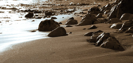 Smooth rocks dot the sandy shoreline as gentle waves lap against the beach during a tranquil...