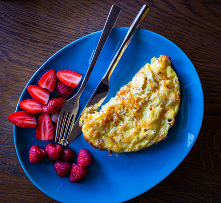 A feta cheese omelet placed on blue plate garnished with strawberries and raspberries