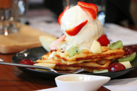 Ice cream on top of wafers and toppings with fruit such as strawberries, kiwi, grapes, and apples, with honey.の写真素材