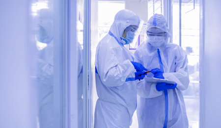 Asian woman doctor in personal protective suit with mask writing on quarantine patient chart,...