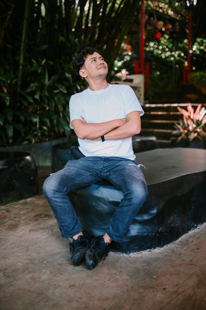 A Southeast Asian man sits with his arms crossed, exuding a relaxed yet confident demeanor. Perfect...