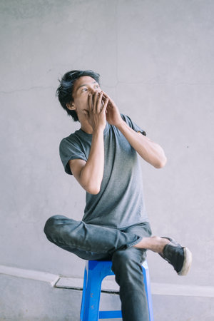 A Southeast Asian man covering his mouth with both hands, conveying surprise or a moment of...