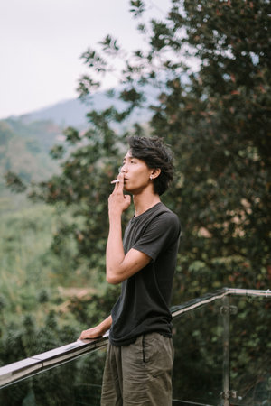 A Southeast Asian man smoking a cigarette, captured in a relaxed moment, with subtle details of the smoke visibleの写真素材