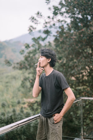 A Southeast Asian man smoking a cigarette, captured in a relaxed moment, with subtle details of the smoke visibleの写真素材