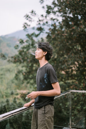 A Southeast Asian man smoking a cigarette, captured in a relaxed moment, with subtle details of the smoke visibleの写真素材