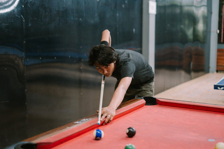 A Southeast Asian man playing billiards, focused on aiming the cue ball during a game, captured in a relaxed and engaging setting.の写真素材
