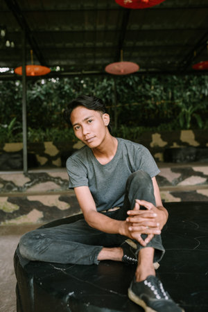 A Southeast Asian man sitting on a stone bench, resting his feet on a nearby chair, appearing relaxed and casualの写真素材