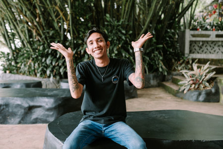 A Southeast Asian man with tattoos sitting and smiling, exuding a relaxed and friendly vibeのeditorial素材