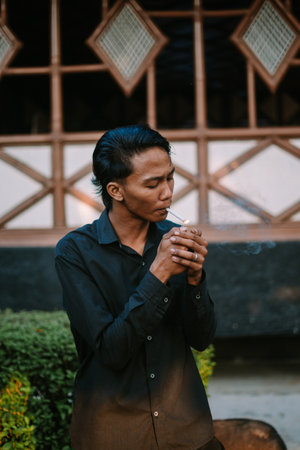 Southeast Asian man lighting a cigarette, focused on the act of smoking.の写真素材
