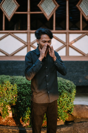 A Southeast Asian man in mid-sneeze, captured with a natural expression.の写真素材