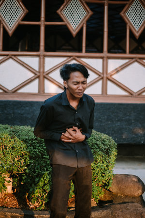 A Southeast Asian man holding his stomach in discomfort, showing signs of abdominal pain.の写真素材