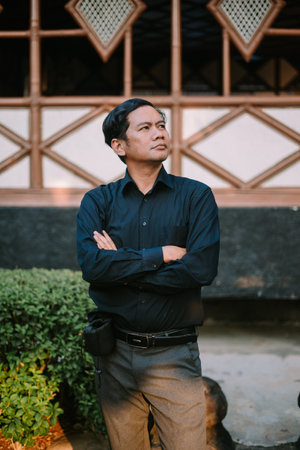 Southeast Asian man crossing his arms, displaying a calm and confident stance. Ideal for themes of authority, confidence, or thoughtful contemplation.の写真素材