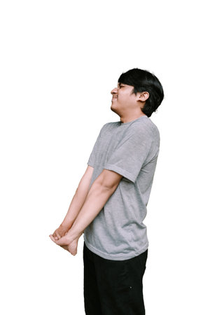 Southeast Asian man stretching his back while appearing relieved, showcasing a moment of comfort. Ideal for themes of relaxation, stretching, and wellnessの写真素材