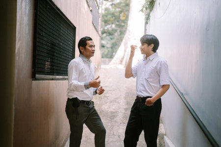 Two Southeast Asian men engaged in a discussion outdoors, standing in a professional setting with a relaxed and collaborative atmosphereの写真素材