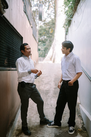 Two Southeast Asian businessmen engaged in a business discussion outdoors, standing in a professional setting with a relaxed and collaborative atmosphereの写真素材