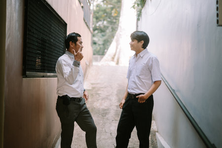 Two Southeast Asian businessmen engaged in a business discussion outdoors, standing in a professional setting with a relaxed and collaborative atmosphereの写真素材