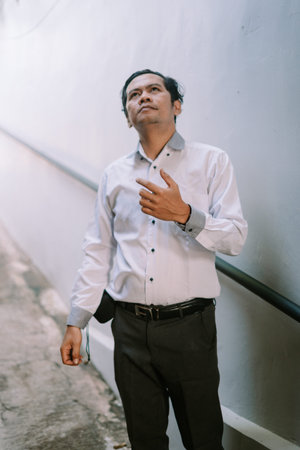 A Southeast Asian man deep in thought, with a contemplative expression, sitting quietly in a casual...