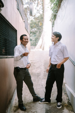 Two Southeast Asian businessmen engaged in a business discussion outdoors, standing in a professional setting with a relaxed and collaborative atmosphereの写真素材