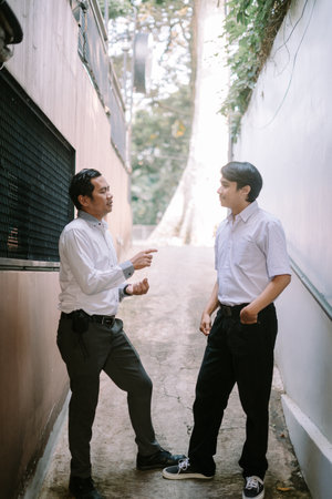 Two Southeast Asian businessmen engaged in a business discussion outdoors, standing in a professional setting with a relaxed and collaborative atmosphereの写真素材