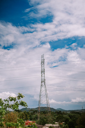 A tall transmission tower against a vibrant blue sky with fluffy white clouds.の写真素材
