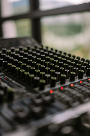 Close-up view of a sound mixer with numerous knobs and faders, ideal for music production or audio...