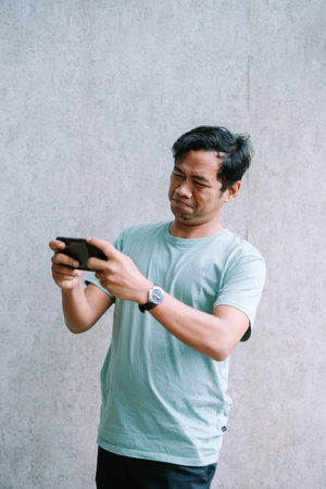 Asian man concentrating intensely while playing a game on his smartphone.の写真素材