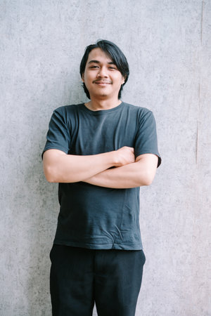 Confident young man standing with arms crossed, wearing a black t-shirt.の写真素材