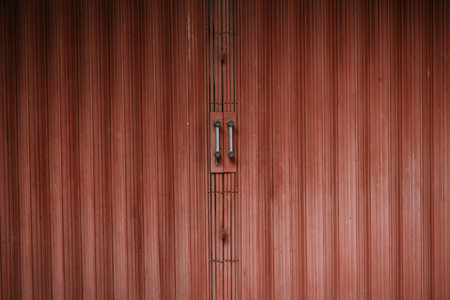 Close-up of a weathered red rolling shutter door with metal handles, adding a vintage industrial touch.の写真素材