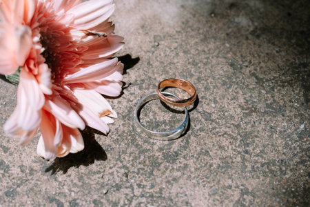 Wedding rings beside a delicate pink flower on a textured surface.