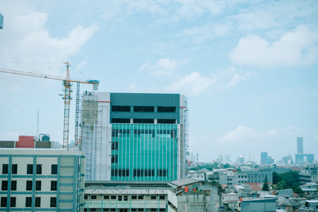 A modern building under construction with a crane and scaffolding against a cloudy sky.の写真素材