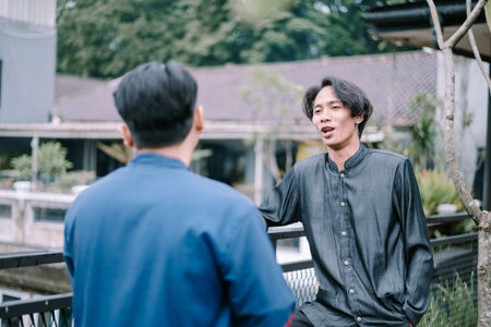 Two young men are seen engaged in conversation outdoors. The individuals are casually dressed,...
