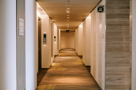 Hotel hallway featuring a long corridor with a carpeted floor. The design includes recessed lighting, creating a perspective view of the interior architecture. An inviting space with an aesthetic that evokes a sense of comfort and refined design.の写真素材