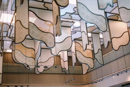 A modern and artistic ceiling decoration featuring textured panels suspended from contoured metal frames. This eye-catching installation combines geometric shapes and neutral tones to create an elegant, abstract design, perfect for upscale interiors or architectural projects.の写真素材