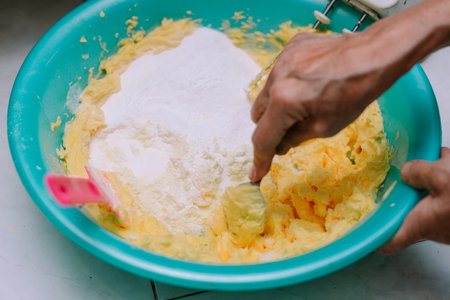 Close-up shot of someone mixing flour into batter inside of a blue bowl, ready for the baking process. It shows someone making homemade cake. An intimate depiction of culinary work, it is an ingredient preparation for making a sweet dish.の写真素材