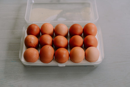 A dozen fresh brown eggs neatly arranged in a clear plastic container, resting on a wooden surface....