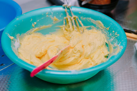 A close-up showcases a turquoise bowl containing smooth, pale yellow cake batter, partially mixed with a whisk and spatula. This image captures a moment in home baking, hinting at the preparation for a sweet and delicious dessert.の写真素材