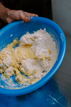 Closeup of person mixing dough ingredients in a bright blue bowl. Flour and wet ingredients are being combined for making a homemade pastry or bread. Culinary concept, preparing food in a domestic setting.の写真素材