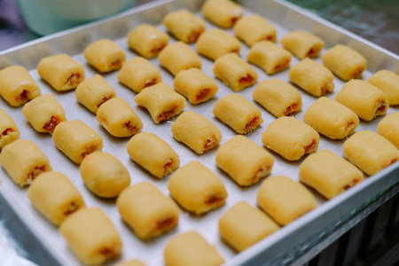 Close-up shot of rows of uncooked pineapple tart cookies on a silver baking tray. These bite-sized treats offer a taste of home-baked goodness, their golden crusts promising a delightful sweetness.の写真素材