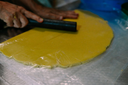 A person is rolling a vibrant yellow dough on a plastic film, preparing it for a delectable pastry. The skilled hands maneuver the tool with precision, showcasing a dedication to culinary artistry. The texture and smooth surface of the dough evoke a sense of homemade goodness.の写真素材
